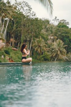 Photo by Gustavo Fring Side view full length of slim unrecognizable brunette in swimwear sitting in lotus pose and meditating while spending time near peaceful pond in tropical country