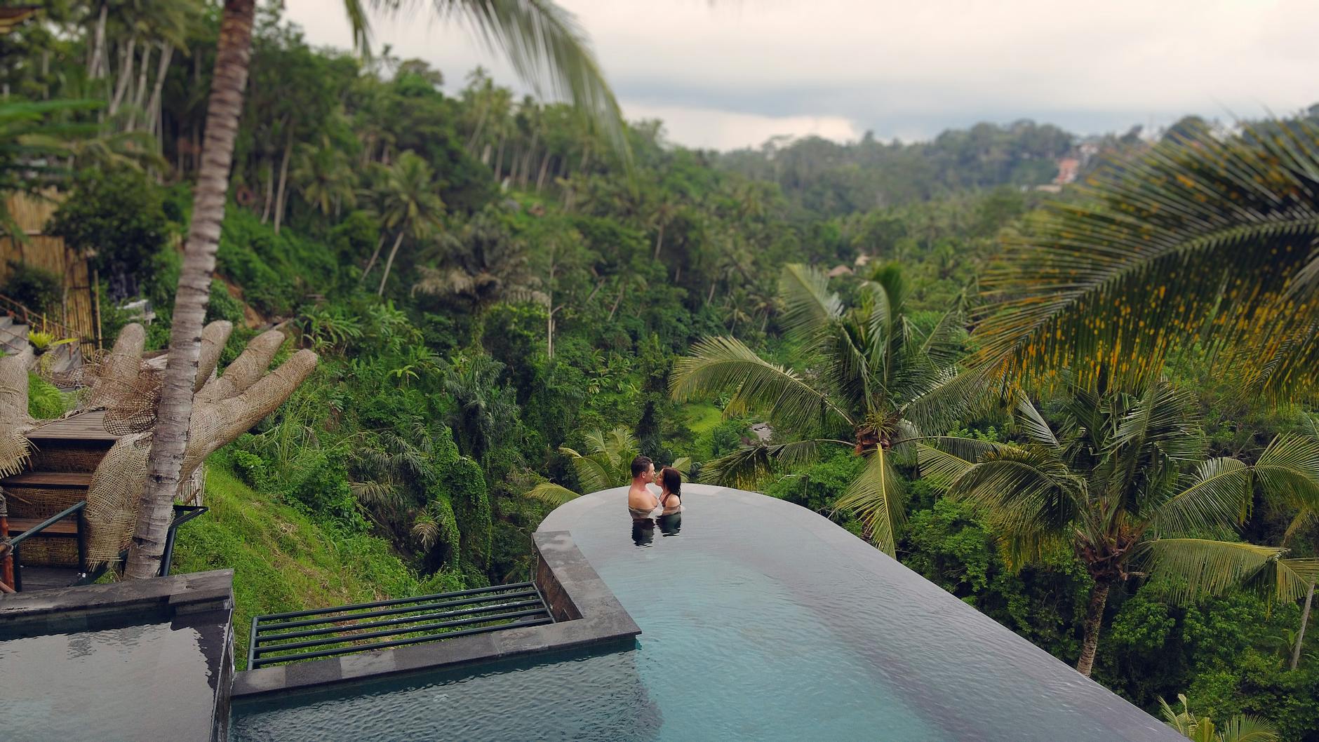 A couple relaxes in a luxurious infinity pool with a breathtaking view of Bali's lush jungle.