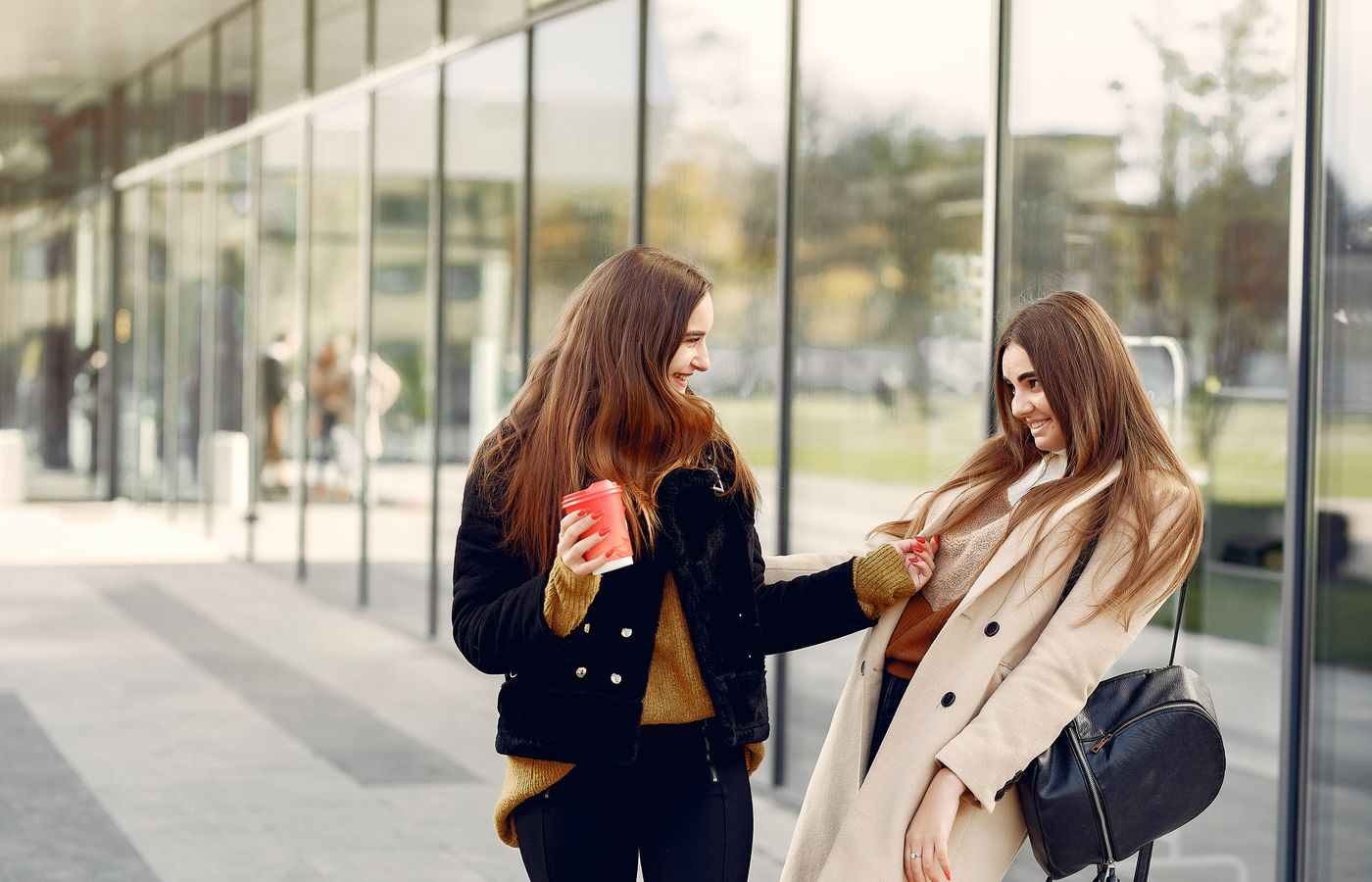 Two young women enjoying a coffee break outdoors, laughing and talking.