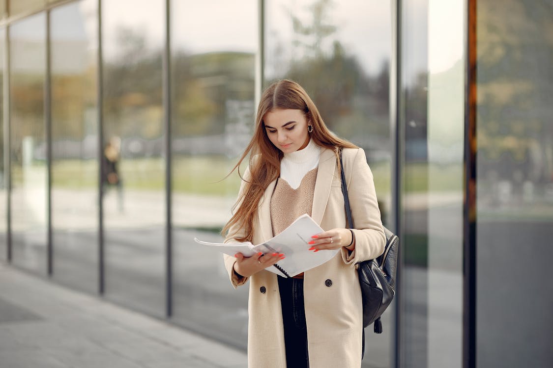 Young woman with clipboard standing near modern building