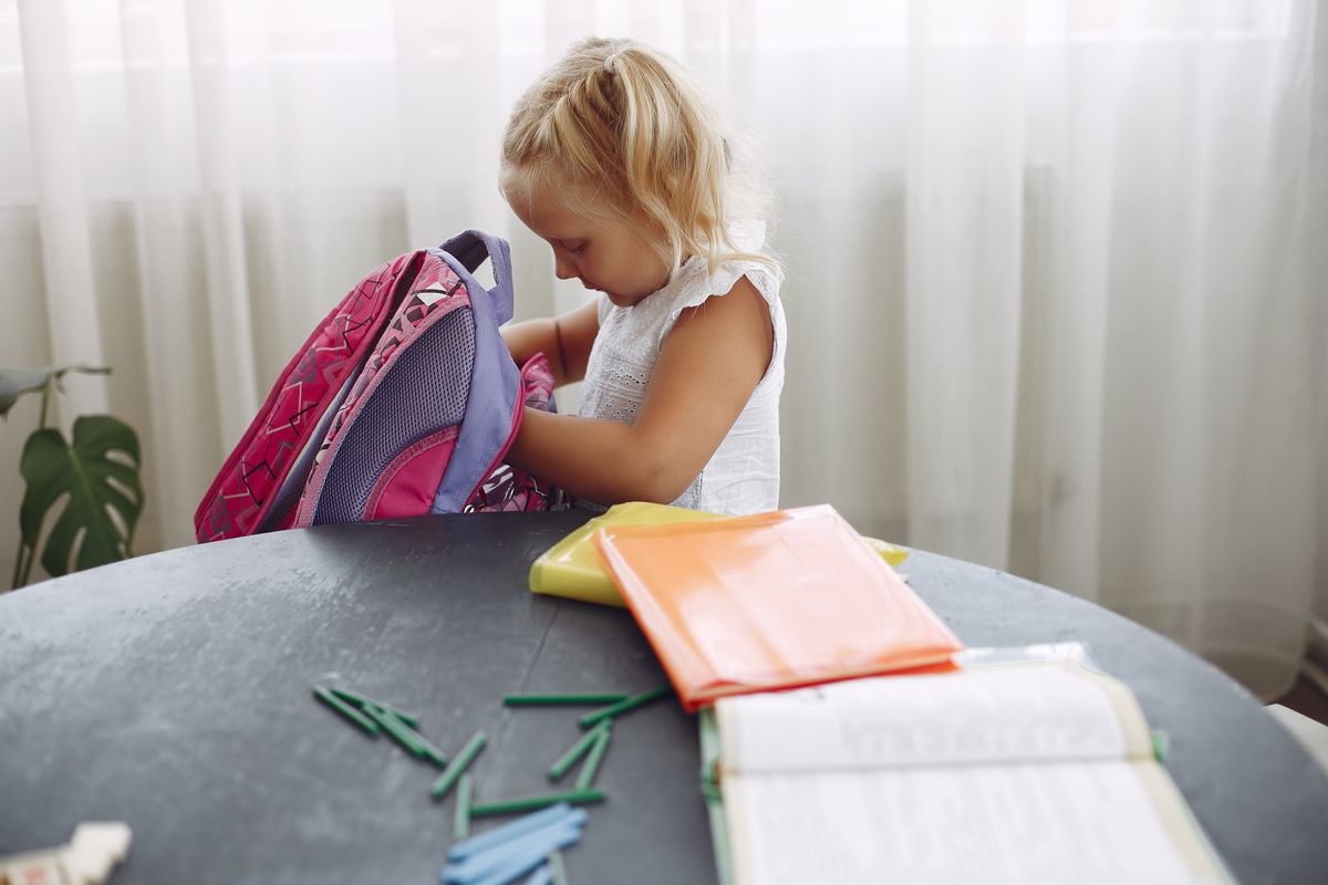 Young girl packing her backpack at a table at home