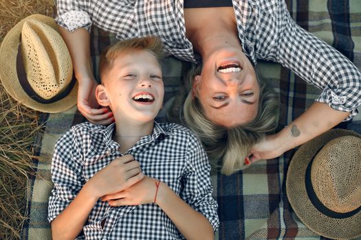 Top view of cheerful mother with som smiling and looking at camera while resting together on blanket