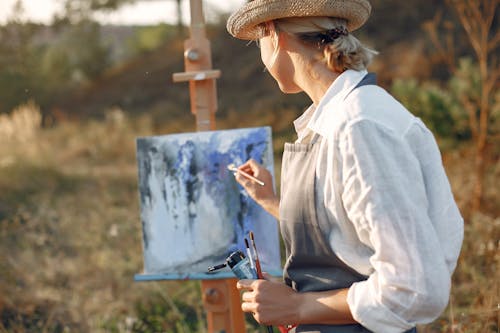 Anonymous woman in hat painting in field