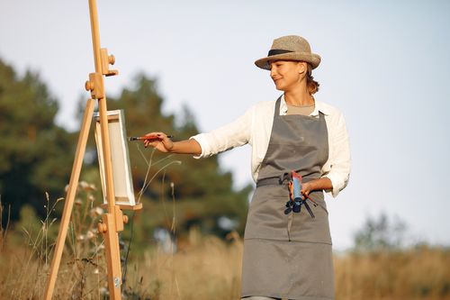 Free Cheerful woman in hat and apron painting while standing in summer sunny day on middle of field Stock Photo