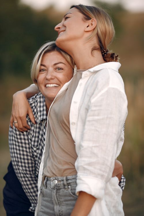 Free Cheerful women wearing casual clothes embracing each other while standing in field and enjoying time together in summer day during weekend Stock Photo