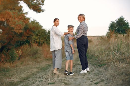 Back view of delighted adult mother and preteen son strolling together with middle age grandmother on path in summer field during weekend in countryside while looking over shoulder