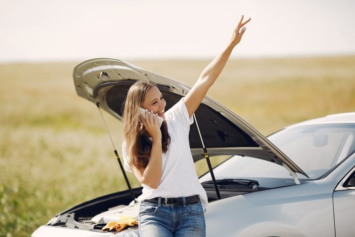 Cheerful young female driver in white t shirt and jeans speaking on phone and looking away with smile