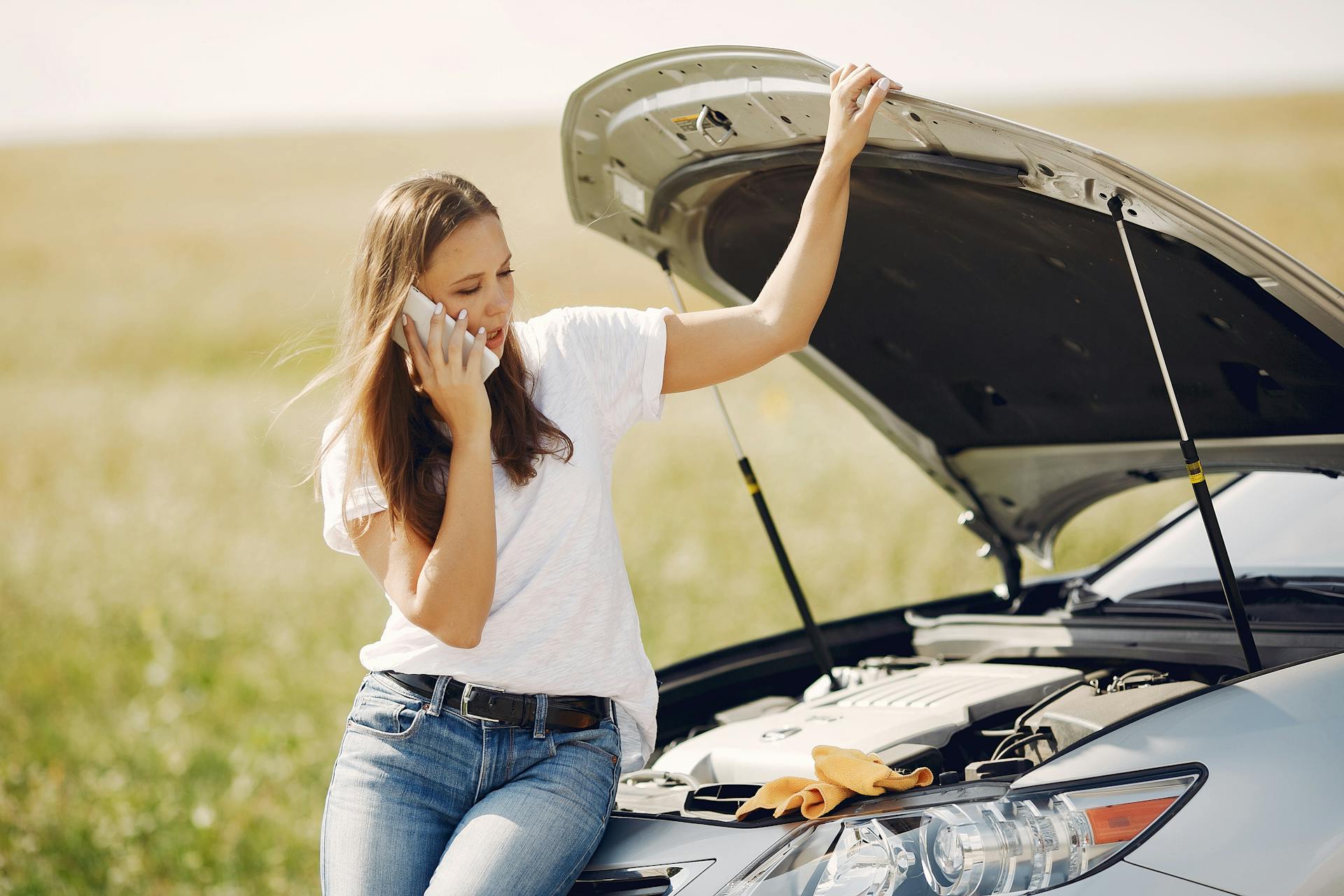 Young woman on phone seeking help for car breakdown on a sunny day.