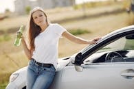 Content young woman with refreshing drink near modern automobile during car trip