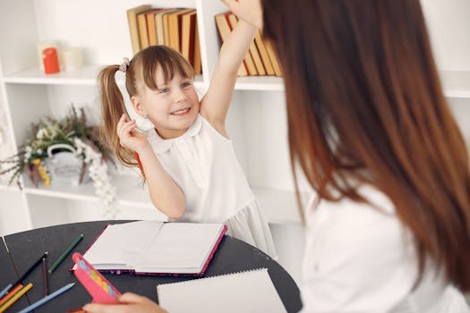 Cheerful child in a classroom raising hand during a learning session with teacher.
