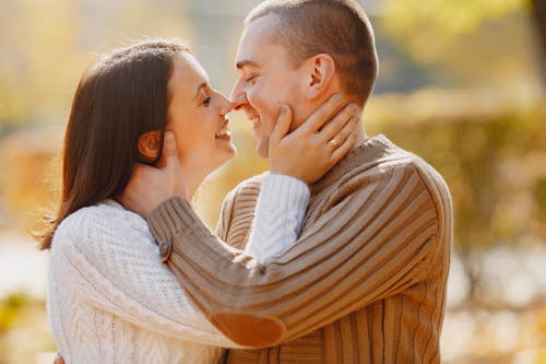 Side view of adult husband and wife hugging and kissing each other with closed eyes while standing close to each other during romantic date in park