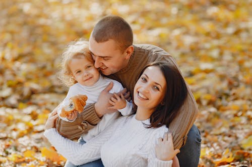 Happy parents with cute daughter strolling in park in autumn day