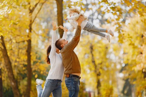 Free Side view of happy young parents standing close to each other while playing with cute little daughter throwing up and catching child with raised arms Stock Photo
