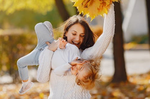Joyful mother and daughter playing in autumn park