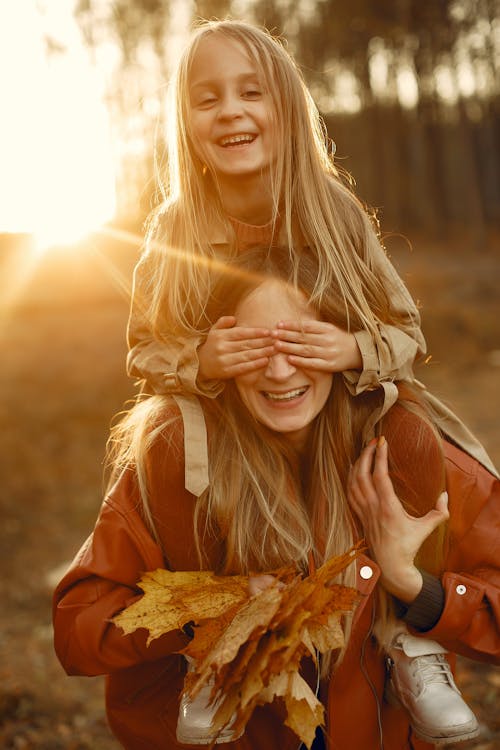 Happy mother piggybacking little daughter in forest