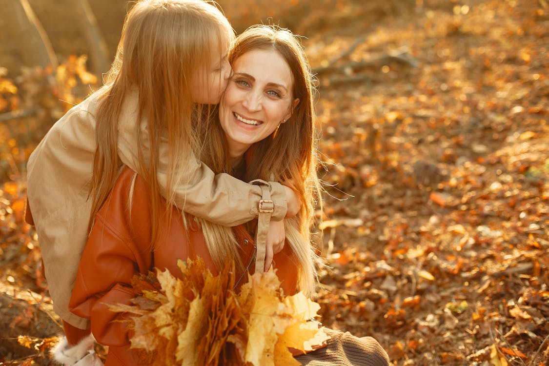 Happy daughter kissing mothers cheek in autumn sunset park