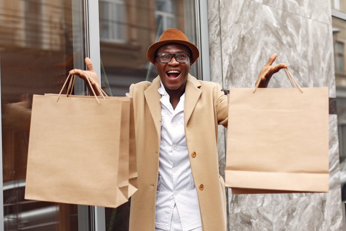 Excited man showing shopping bags near marble wall