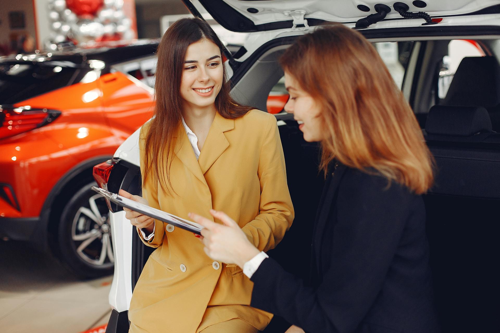 Two women engaged in a conversation about purchasing a car in a dealership showroom.