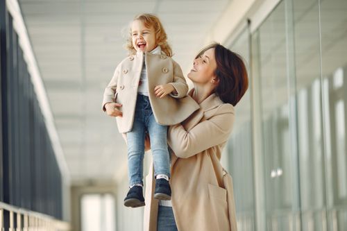 Free Happy content woman in stylish outfit with cheerful laughing daughter on shoulder smiling and  standing in contemporary urban hall in daylight Stock Photo