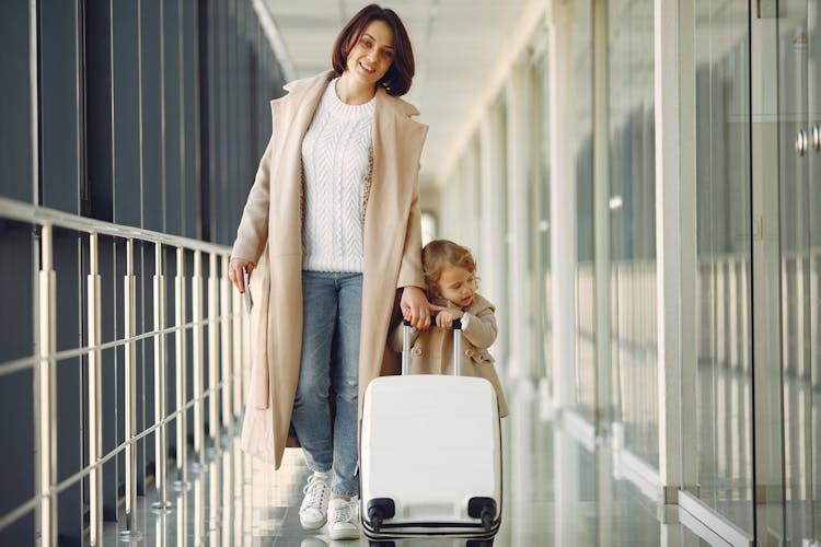 Positive Mother And Daughter With Suitcase In Airport Corridor