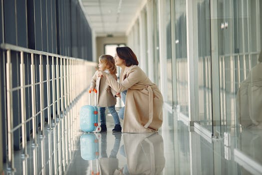 Side view full body of astonished cute little girl with kids suitcase and smiling mother pointing out window while walking together in contemporary airport hallway