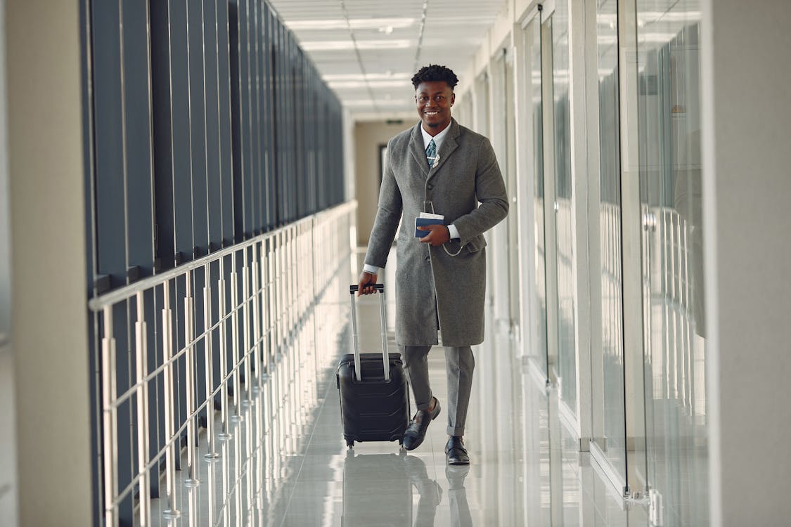 Stylish man with suitcase and passport walking along airport corridor ·  Free Stock Photo