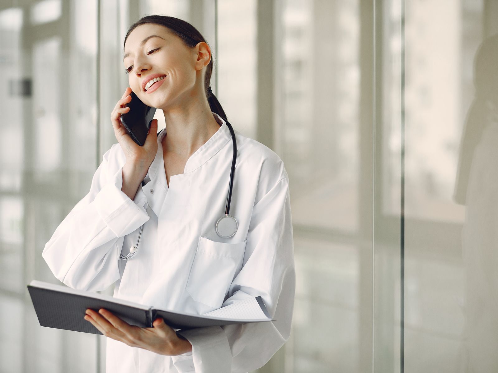 Friendly doctor speaking on a phone while holding a notebook in a clinic
