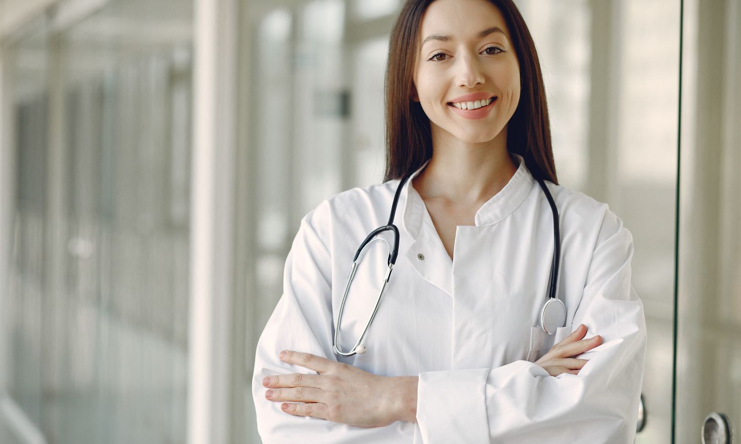 Doctora con bata blanca y fonendoscopio en un pasillo de hospital