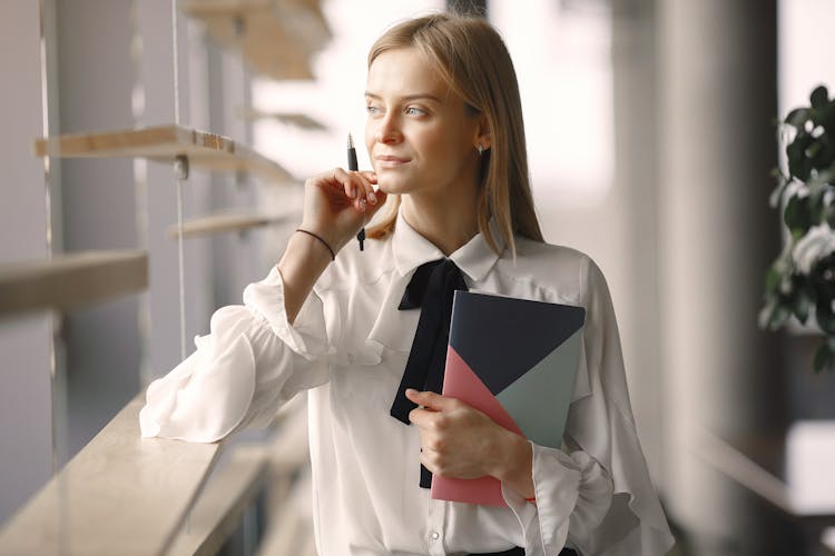 Thoughtful Worker With Notebook And Pen In Office Lobby