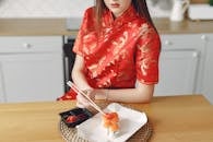 一位身着红色连衣裙的亚洲妇女正在木桌上用筷子享用寿司