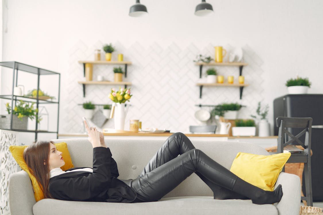 Young woman with smartphone lying on sofa in living room