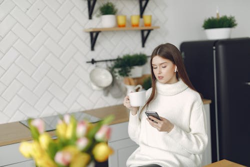 Young woman with smartphone and coffee in kitchen