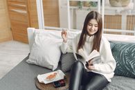 女人在舒适现代的生活空间里，一边享受寿司，一边阅读书籍