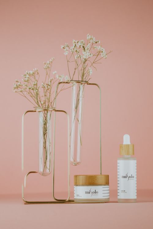 Free Stylish studio shot of skincare products with delicate flowers against a peach background, perfect for beauty promotions. Stock Photo