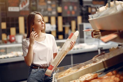 Positive young lady choosing baguette in market