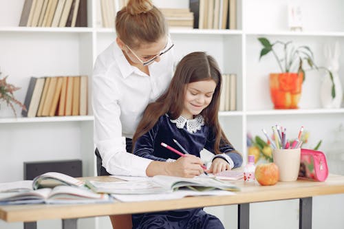 Free Cheerful schoolgirl doing homework with teacher in classroom Stock Photo
