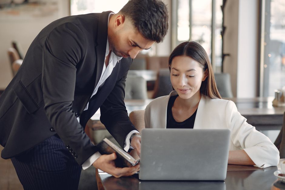 Concentrated multiethnic male and female in formal wear with notebook and laptop discussing business project while working in creative workspace