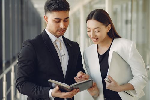 Free Focused diverse coworkers in formal clothes with notebook and laptop in hands standing in hall and discussing business project together Stock Photo