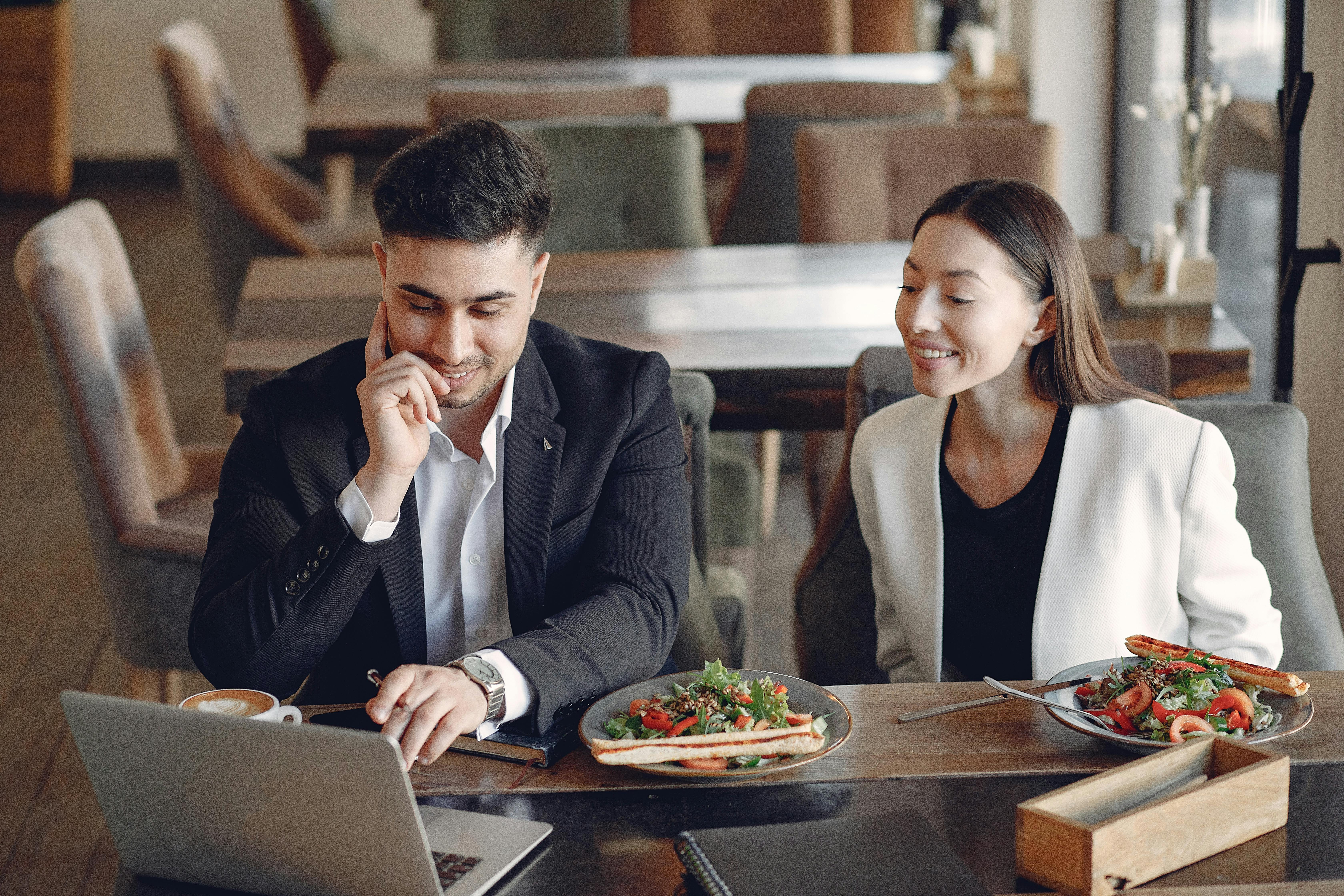 Smiling multiracial business partners in formal wear sitting in cafe while working on project and using laptop
