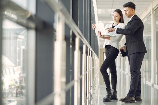 Low angle side view of focused multiethnic colleagues in formal suits standing near window in modern office and using laptop while discussing business