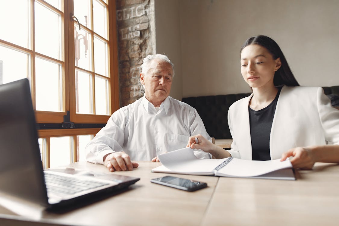 Free Focused elegant senior man and adult woman in smart casual outfit working on project with laptop and notes together in modern workspace Stock Photo