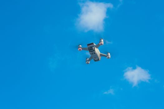 Low angle of white modern drone with photo camera and propellers against blue sky with rare clouds