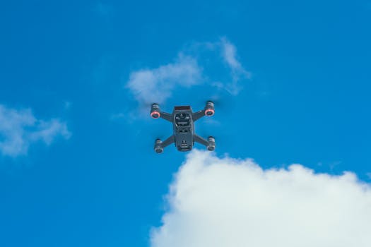 A modern quadcopter drone navigating through a bright blue sky with clouds. Ideal for tech and innovation themes.