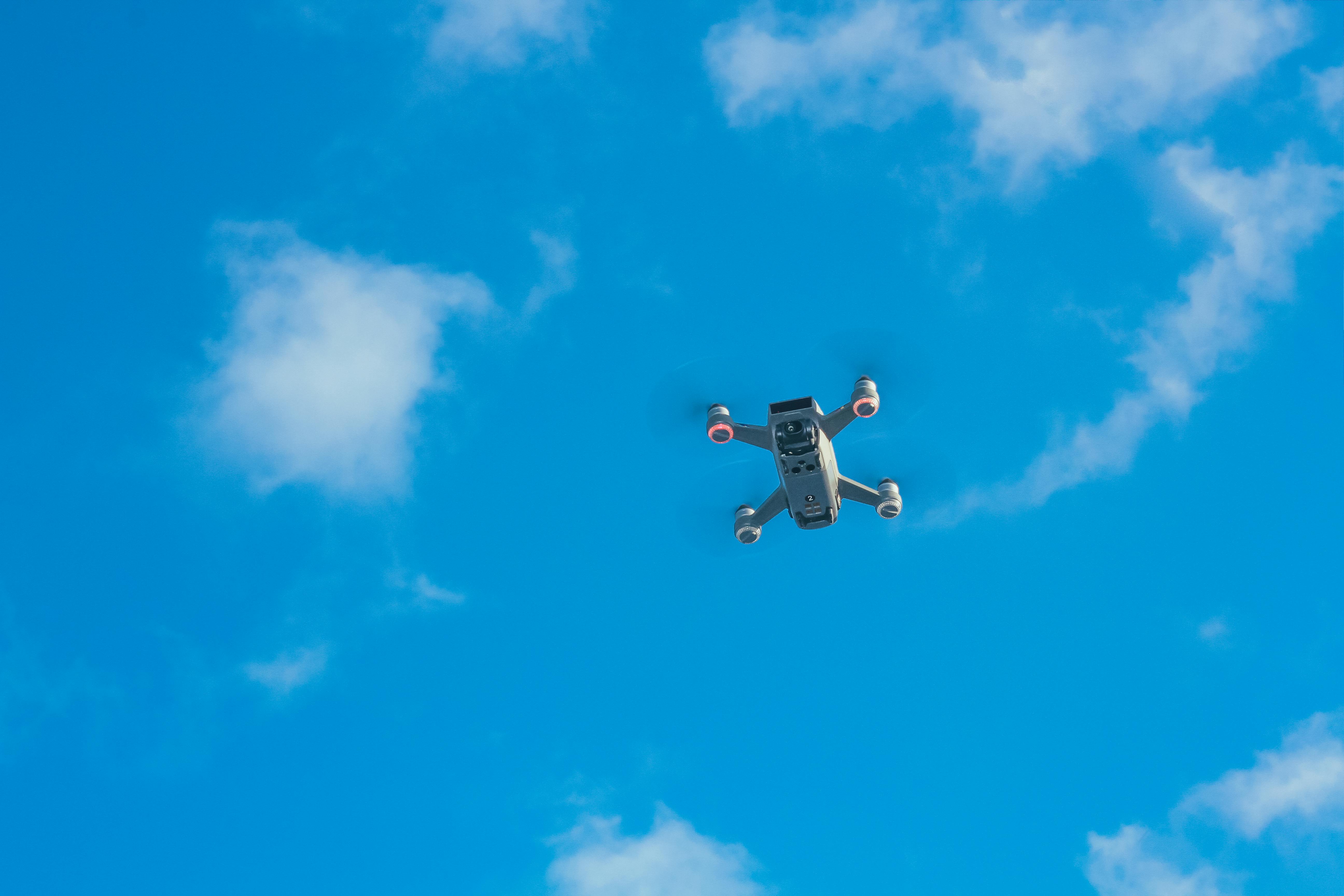 From below of modern UAV with small lightning round elements and quickly spinning propellers against vibrant blue sky with clouds