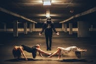 Full body of unrecognizable male in black closing rising arms while making to fly slim charming women in dresses