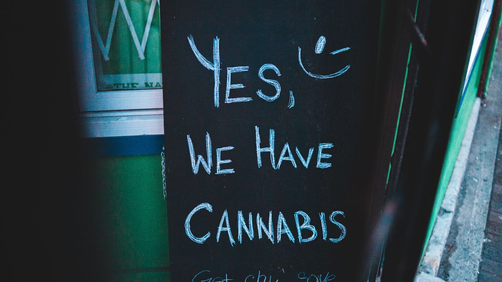 Lettering written on black chalkboard with cannabis offer near house on street of city