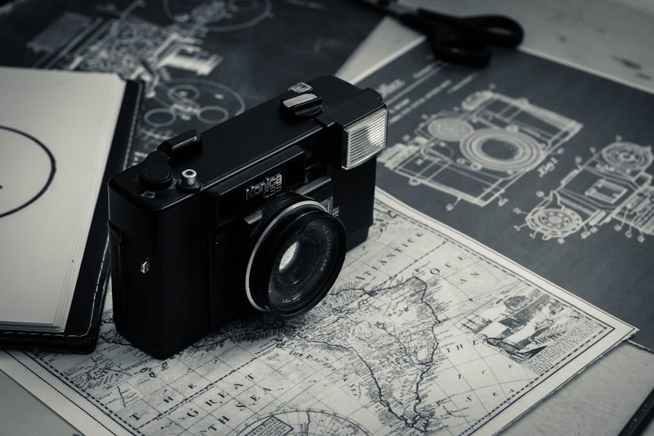 From above of black and white vintage film camera laced on table with map and notebook