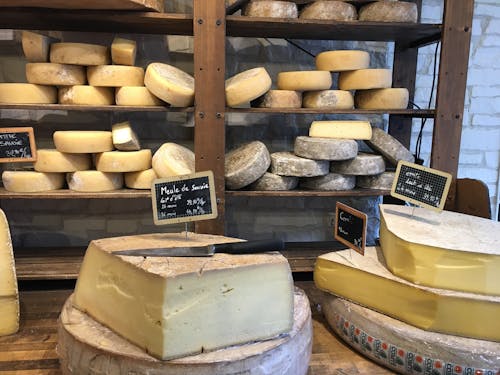 チーズの上にナイフが置いてあり奥の棚には多くのチーズがある画像