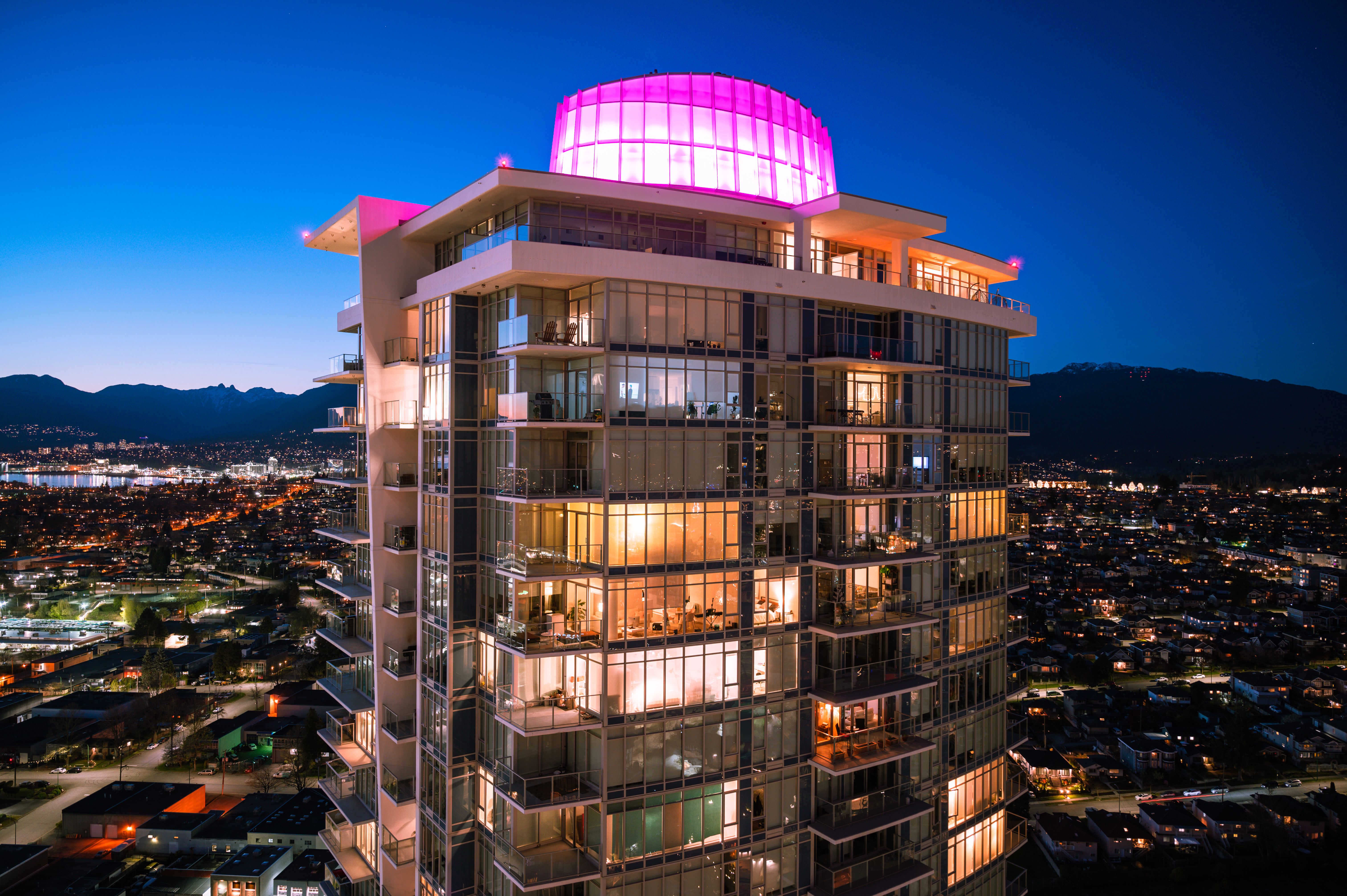 Stunning view of a lit skyscraper in Burnaby, BC during twilight with cityscape backdrop.