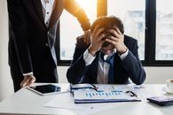 明亮的办公室里，一位商人不知所措地捂着头，周围堆满了报告